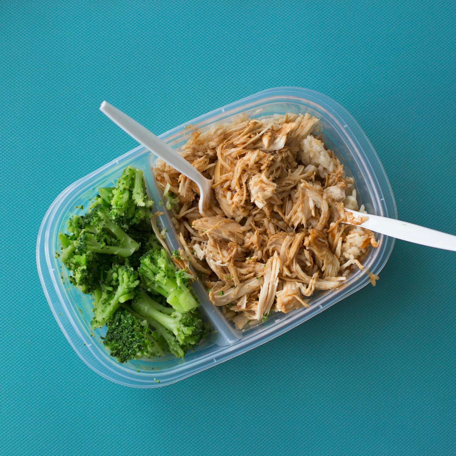 Hand sprinkling fresh herbs onto a chicken and rice meal prep box